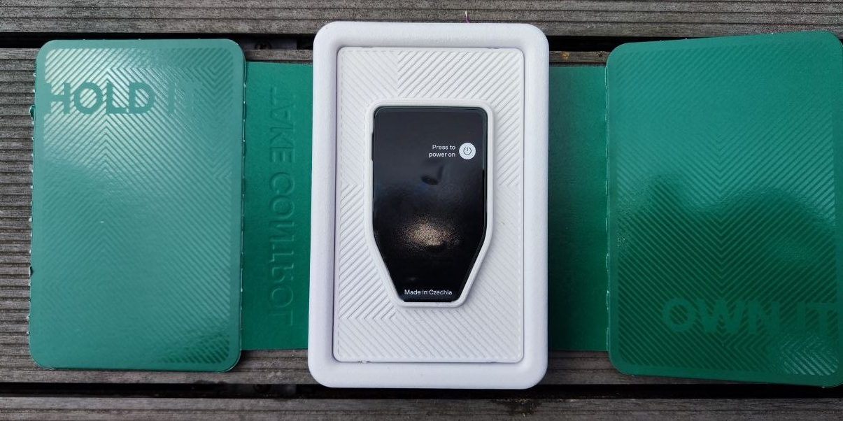 Trezor Safe 7 Hardware Wallet mit Verpackung und grünem Zubehör für die sichere Offline-Verwahrung von Kryptowährungen.