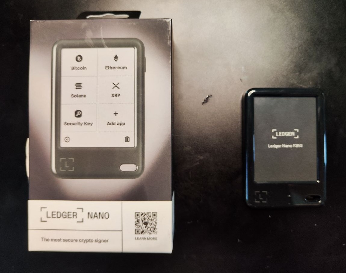 Ledger Nano 5 neben der Originalverpackung während des Einrichtungsvorgangs mit eingeschaltetem Display