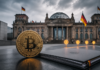 Bitcoin-Münze vor dem Reichstagsgebäude neben einer Akte zur geplanten Krypto-Steuer in Deutschland