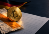 Bitcoin-Münze auf Kaufbelegen und einem Steuerformular vor den deutschen Farben