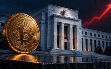 FED-Zinserhöhung fast sicher: Warum Bitcoin trotzdem steigen könnte Goldene Bitcoin-Münze vor der US-Notenbank mit rotem Pfeil für steigende Zinsen