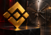 Goldenes Binance-Logo vor einer geschlossenen Tresortür auf dunklem Hintergrund mit roten Lichtakzenten.