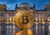 Goldene Bitcoin-Münze vor dem beleuchteten Reichstagsgebäude in Berlin.