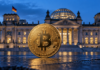 Goldene Bitcoin-Münze vor dem beleuchteten Reichstagsgebäude in Berlin zur blauen Stunde.