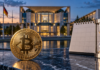 Krypto-Haltefrist: Abschaffung offenbar vor dem Aus – Schäffler enthüllt Kabinettsplanung Goldene Bitcoin-Münze neben Kalender und Sanduhr vor dem Bundeskanzleramt in Berlin.