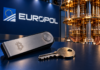 Bitcoin-Hardware-Wallet und metallischer Schlüssel vor einem Quantencomputer und einem Europol-Logo.