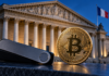 Hardware-Wallet und Bitcoin-Münze vor der französischen Nationalversammlung mit französischer Flagge.
