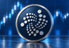 Großes IOTA-Logo auf einer dunkelblauen Münze vor einem abstrahierten Kurschart.