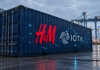 Symbolischer Frachtcontainer mit H&M-Logo und digitalen Datenverbindungen in einem Logistikterminal.