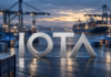 Silberner IOTA-Schriftzug vor einem Containerhafen mit blauen digitalen Datenverbindungen.