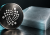Metallisches IOTA-Logo neben einem Stapel transparenter Zertifikate vor dunklem Hintergrund.