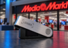 Ledger-Hardware-Wallet vor einer MediaMarkt-Filiale mit rotem Unternehmenslogo.
