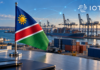 Namibische Flagge vor einem Containerhafen mit digitalen Verbindungslinien und IOTA-Logo.