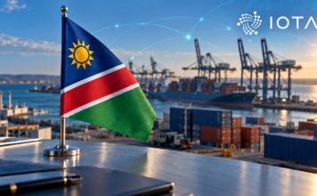 Namibische Flagge vor einem Containerhafen mit digitalen Verbindungslinien und IOTA-Logo.