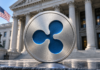 BREAKING: Ripple erhält Bankzulassung in den USA – historischer Meilenstein erreicht Silbernes Medaillon mit blauem Ripple-Logo vor einer Bankfassade mit US-Flagge.