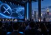 Ereignisreiche Woche steht für Ripple bevor: Kann der XRP-Kurs profitieren? Ripple Swell 2026 in New York: XRP-Symbol auf großer Leinwand vor Konferenzteilnehmern und der Skyline von Manhattan.