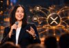 Ripple-Präsidentin Monica Long bei einem Vortrag vor einer Illustration des XRP-Logos und eines globalen digitalen Zahlungsnetzwerks.