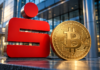 Rotes Sparkassen-Logo neben einer goldenen Bitcoin-Münze vor einer modernen Bankfassade.