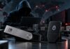 Symbolbild zum Ledger-Skandal: Ledger- und Trezor-Hardware-Wallets im Vordergrund, dahinter ein vermuteter Hacker mit Laptop sowie angedeutete Lieferketten- und Cyberangriffs-Szenerie.