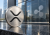Silberne Münze mit XRP-Symbol vor einer Glasfassade mit Ripple-Logo.